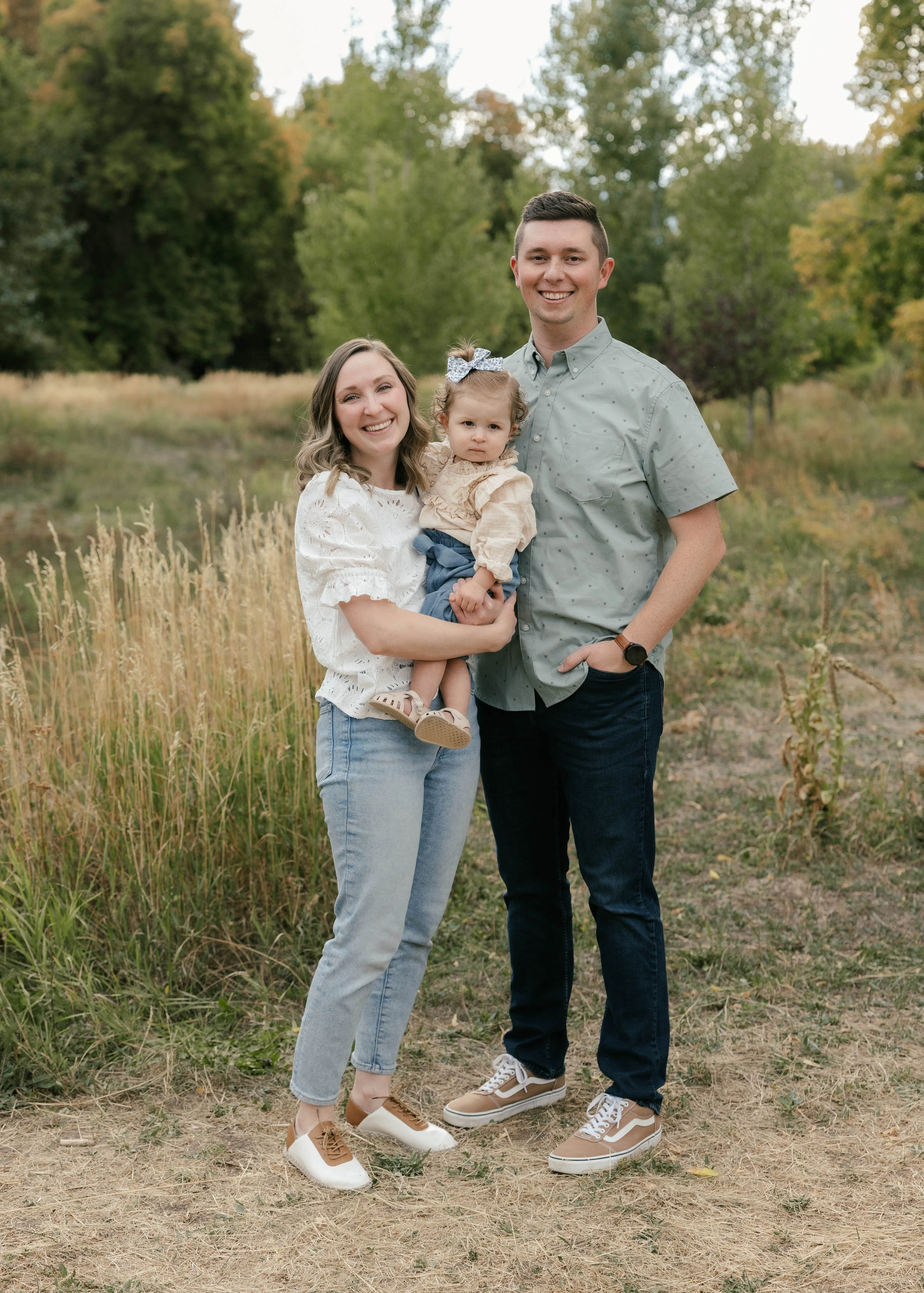 Jace Cox outdoors with his wife and their young child, all three smiling.